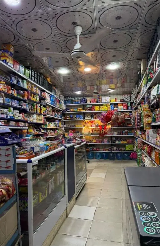Inside Dukan Near Me: well-stocked shelves of snacks, drinks and household goods under the shop's decorated ceiling, with gift balloons at the back